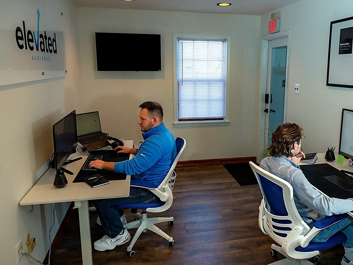 Two Elevated Audience strategists at work in the office, under the Elevated Audience sign
